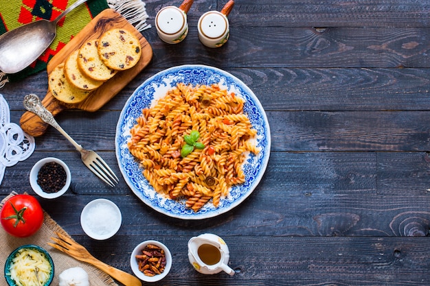 Fusilli à la sauce tomate tomates oignons ail séché olives de paprika poivron et huile d'olive sur un fond en bois. Photo Premium