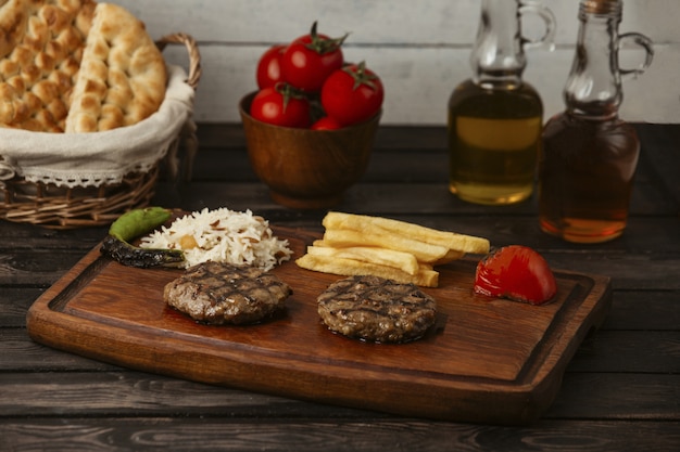 Galettes de boeuf grillées servies avec riz, frites, tomates grillées et poivrons Photo gratuit