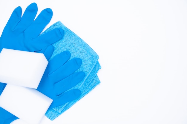 Gants bleus et éponge de chiffon sur blanc. set de nettoyage vue de dessus. pose à plat Photo Premium