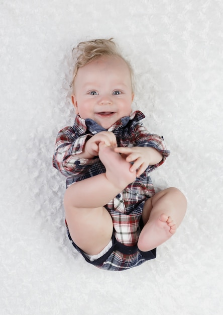 Un Garcon Blond De Six Mois Aux Yeux Bleus Dans Une Chemise A Carreaux Bodik Se Trouve En Jouant Avec Ses Jambes Souriant Mignon Photo Premium