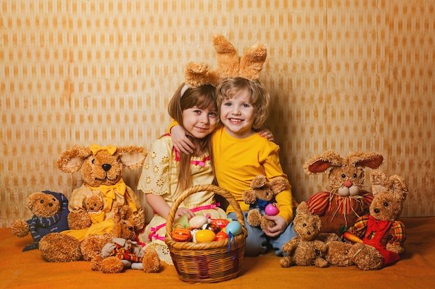 Garçon et fille avec des oreilles de lapin assis autour de beaucoup de paille et de lièvres en peluche, style vintage. Photo Premium