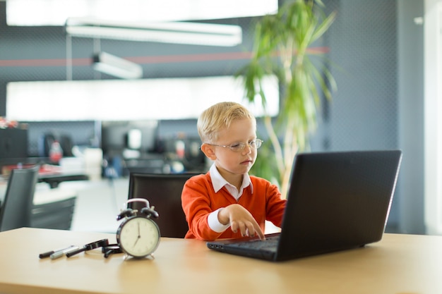 Un garçon mignon s'asseoir au bureau du bureau et utilise un ordinateur Photo Premium