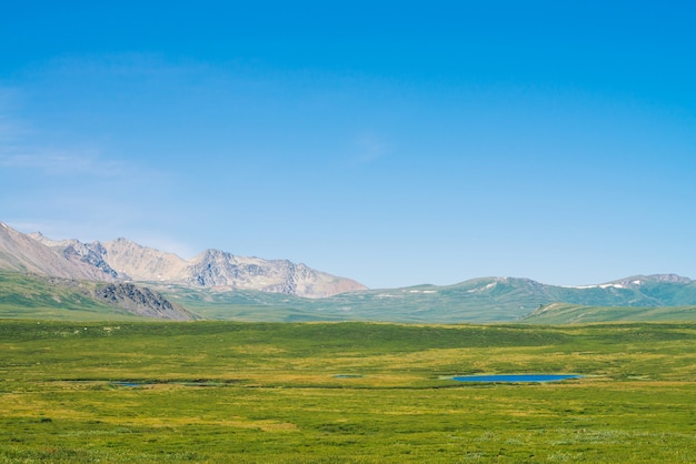 Géant Des Montagnes De Neige Au-dessus D'une Vallée Verdoyante Sous Un Ciel Bleu Clair. Prairie Avec Une Riche Végétation Et Des Lacs De Hautes Terres Au Soleil. Magnifique Paysage De Montagne Ensoleillé De Nature Majestueuse. Photo Premium