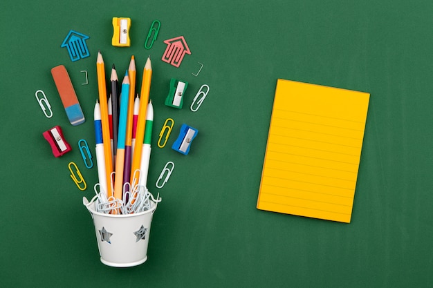 Gomme à effacer pour stylo trombone papeterie crayons dans un seau blanc. nature morte sur fond de commission scolaire verte. espace de copie plat laïque vue de dessus concept education Photo Premium