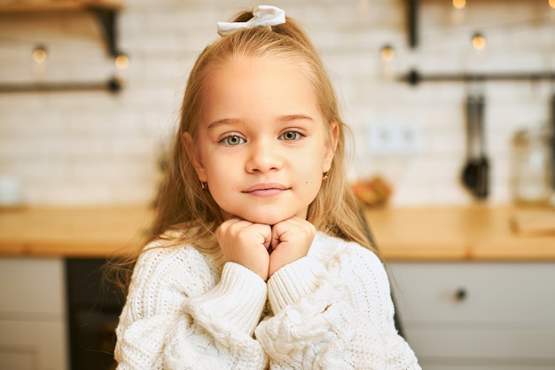 Gros Coup D Adorable Petite Fille Aux Yeux Verts Et Longs Cheveux Laches Tenant La Main Sous Son Menton Avec Sourire Posant Dans La Cuisine Photo Gratuite