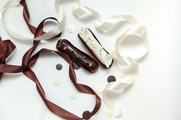 Gros plan, ensemble, deux, éclairs, garnitures différentes, design, décoré, de, gouttes chocolat, ruban soie blanc et marron Photo Premium