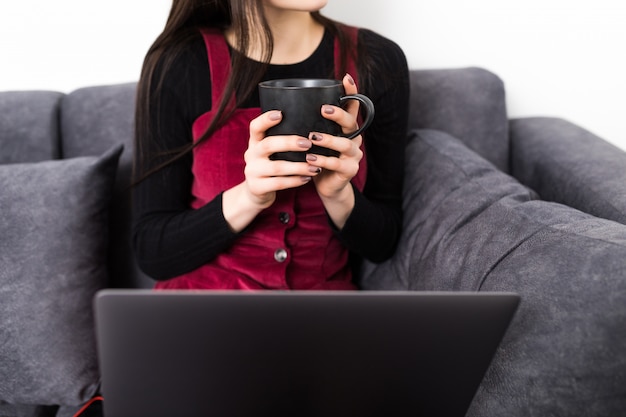 Gros Plan D une Femme Assise Sur Le Canapé Dans Un Salon Et Tenant Une Tasse Tout En Utilisant