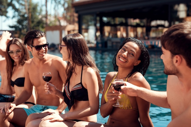 Groupe de jeunes gens heureux assis au bord de la piscine ensemble Photo Premium