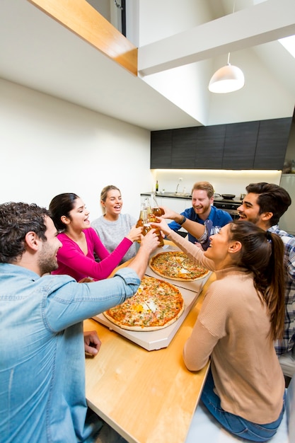 Groupe de jeunes heureux mangeant des pizzas et buvant du cidre dans un intérieur moderne Photo Premium