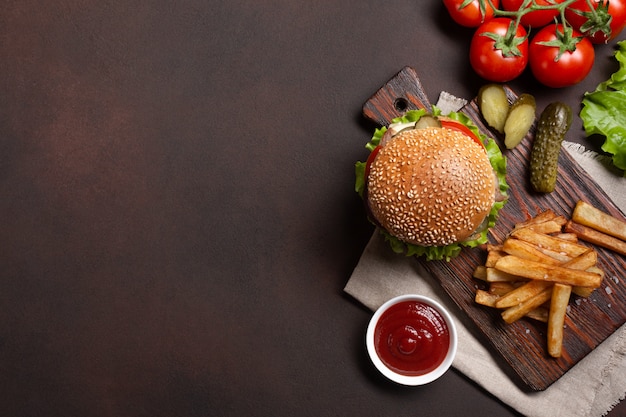 Hamburger fait maison avec du bœuf, des tomates, de la laitue, du fromage, des oignons, des concombres et des frites Photo Premium