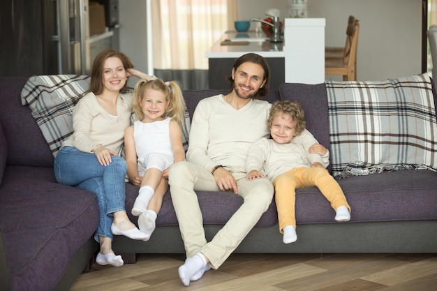 Heureuse famille de quatre personnes assises sur un canapé en regardant la caméra Photo gratuit