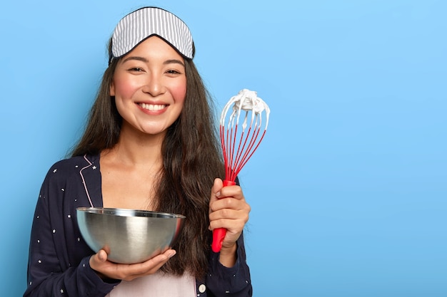 Heureuse Femme Brune Asiatique Fait Un Delicieux Gateau Prepare Un Gateau Fouette Le Blanc D Oeuf Dans Un Bol Avec Batteur Vetu De Vetements De Nuit Masque De Sommeil Photo Gratuite