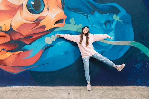 Heureuse femme dansant devant le mur de graffitis colorés Photo gratuit