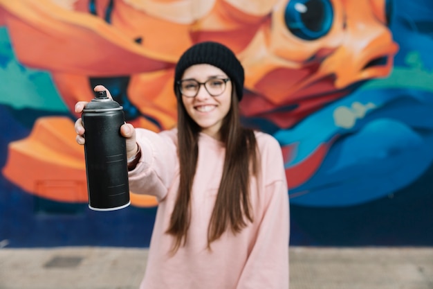 Heureuse femme tenant un flacon pulvérisateur devant le mur de graffitis Photo gratuit
