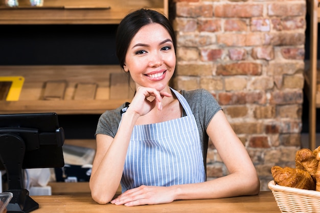 Heureuse jeune femme au comptoir dans une boulangerie en regardant la caméra Photo gratuit