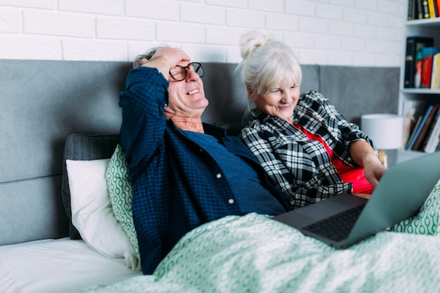 Heureux couple âgé au lit avec un ordinateur portable Photo gratuit