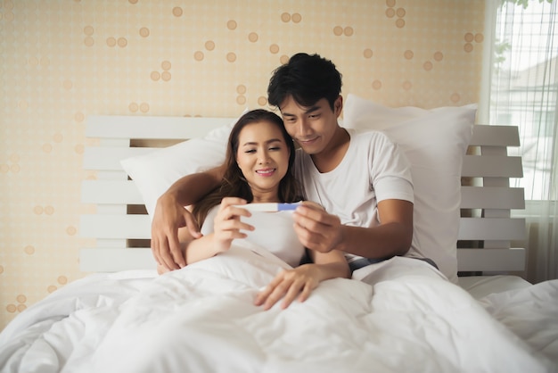 Heureux couple souriant après avoir découvert un test de grossesse positif dans la chambre Photo gratuit
