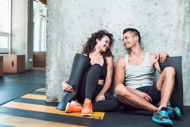Heureux homme et femme avec tapis d'exercice assis dans une salle de sport Photo gratuit