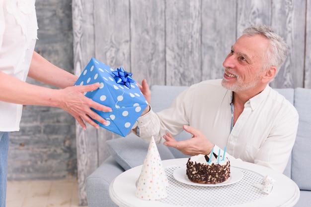 Heureux Homme Recevant Un Cadeau D Anniversaire De Sa Femme Pres De Gateau Et Chapeau De Fete Sur Table Photo Gratuite