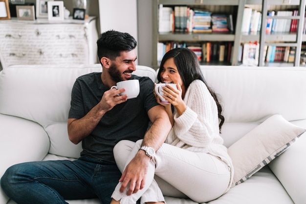 Heureux Jeune Couple Assis Sur Un Canapé Tenant Une Tasse à Café Blanche Photo Gratuite 