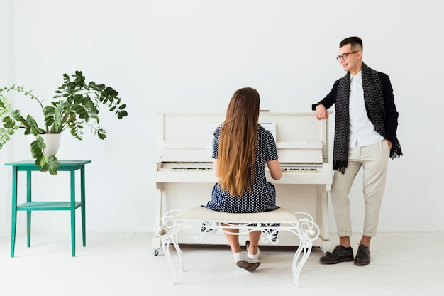 Heureux jeune homme avec la main dans sa poche, regardant la femme jouant du piano Photo gratuit