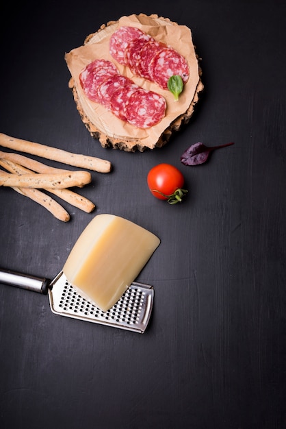 High Angle De Vue De Pepperoni Sur Un Dessous De Verre En Bois Avec Tomate; Des Bâtons De Pain; Fromage Et Râpe Photo gratuit