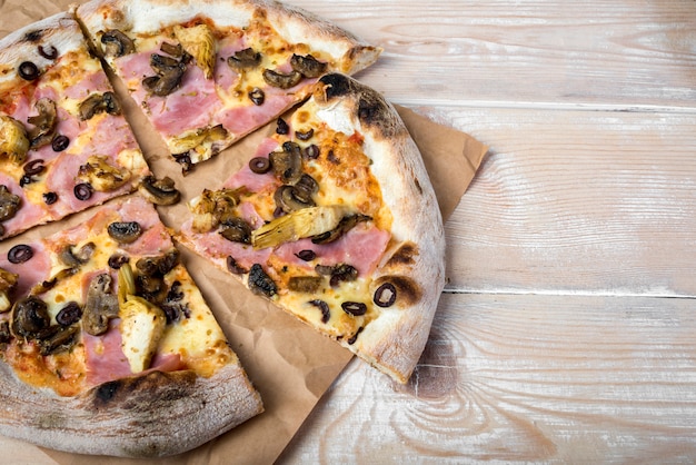 High angle de vue de pizza au pepperoni aux champignons en tranches sur du papier brun au-dessus d'une table en bois Photo gratuit