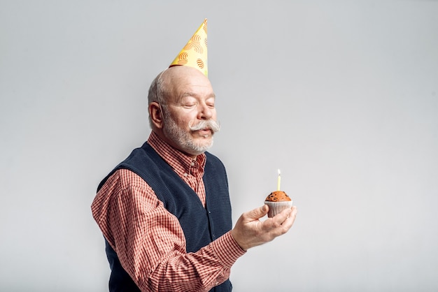 Un Homme Age Souriant Au Chapeau De Fete Montre Un Gateau Avec Une Bougie Joyeux Senior Mature Photo Premium