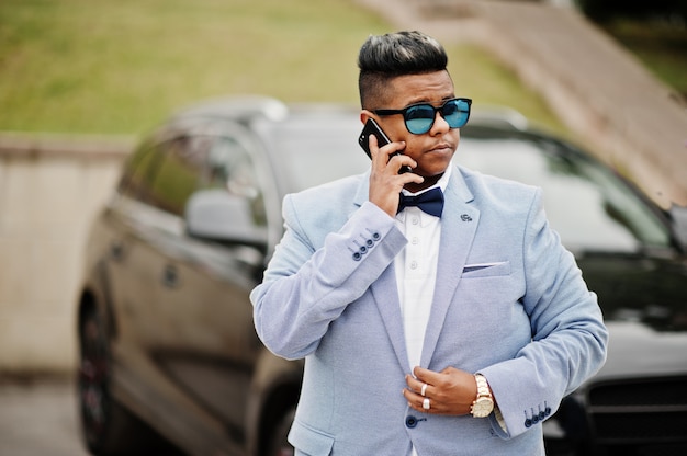 Homme Arabe élégant En Veste, Noeud Papillon Et Lunettes De Soleil Contre Une Voiture Suv Noire. Riche Arabe Parlant Sur Téléphone Mobile. Photo Premium
