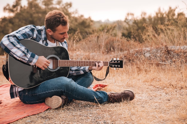 Homme Assis Sur Une Couverture Jouer De La Guitare Photo Gratuite 