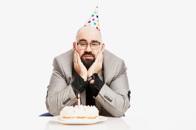 Un Homme Au Chapeau De Clown Est Assis Devant Un Gateau Avec Une Bougie Triste Anniversaire Mur Blanc Photo Premium