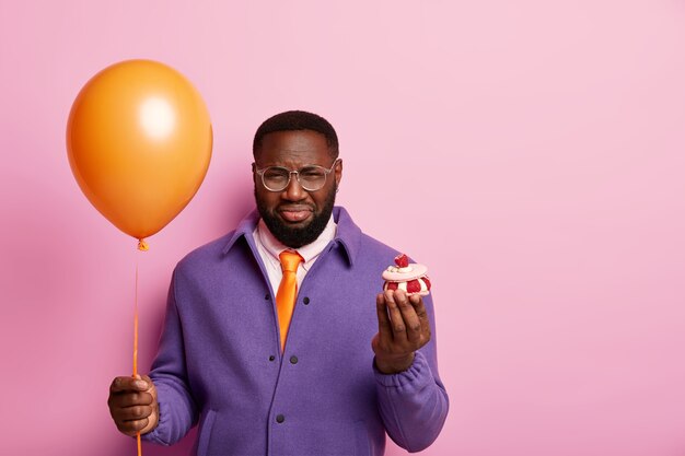 Homme Mecontent Solitaire Bouleverse De Feter Son Anniversaire Seul Se Tient Debout Avec Un Ballon Et Un Gateau Est De Mauvaise Humeur A Cause De Vacances Gatees Porte Une Tenue Violette