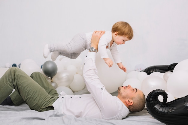 Homme montant petit bébé sur les mains et allongé sur le lit Photo gratuit