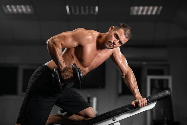 Homme s'entraîne dans le gymnase homme athlétique s'entraîne avec des haltères, pompant son biceps Photo Premium