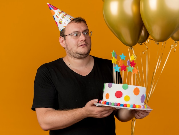 Un Homme Slave Adulte Choque Dans Des Lunettes Optiques Portant Une Casquette D Anniversaire Tient Des Ballons A L Helium Et Un Gateau D Anniversaire Photo Gratuite