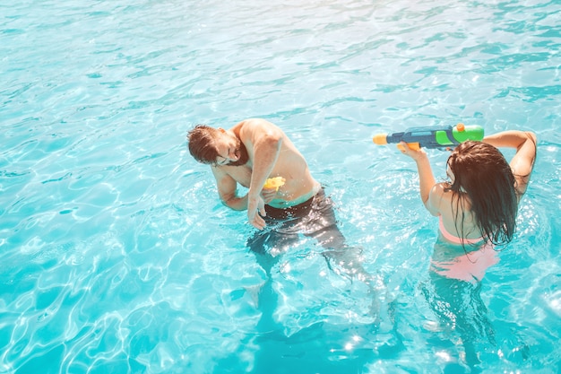 Image Drole De Couple Jouant Dans La Piscine La Fille Tire Dans Le Gars Du Pistolet A Eau Il Essaie De Se Defendre Ils S Amusent Beaucoup Photo Premium