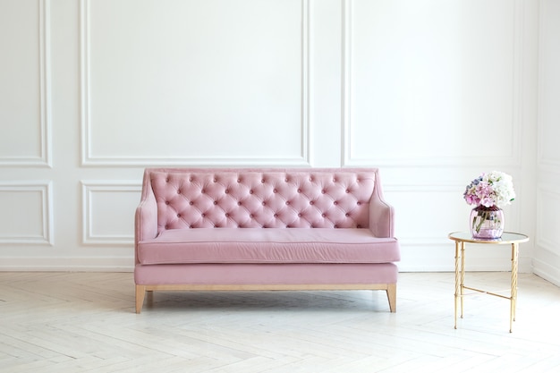 Intérieur de salon minimaliste moderne avec un canapé rose et une table avec un vase de bouquet de fleurs contre un mur blanc. le spacieux salon de style classique dispose d'un canapé en velours. concept de confort Photo Premium