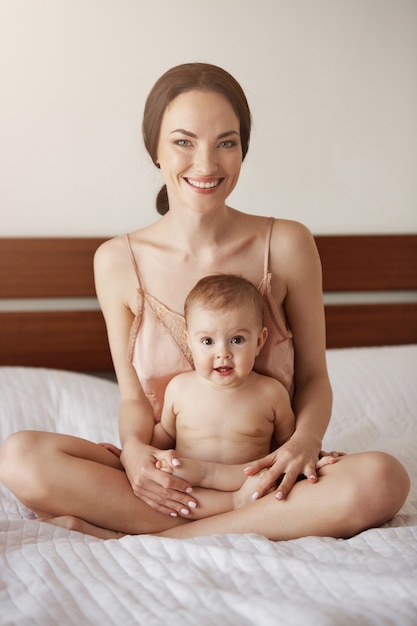 Jeune Belle Maman Heureuse En Vetements De Nuit Et Son Bebe Nouveau Ne Assis Sur Le Lit Le Matin En Souriant Jouant Ensemble Photo Gratuite