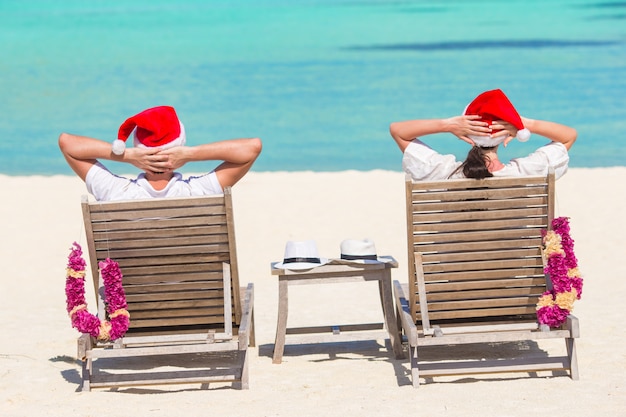 Jeune couple en chapeaux santa se détendre sur une plage tropicale pendant les vacances de noël Photo Premium