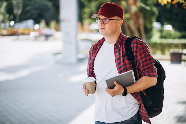 Jeune étudiant, boire du café avec ordinateur portable dans le parc Photo gratuit