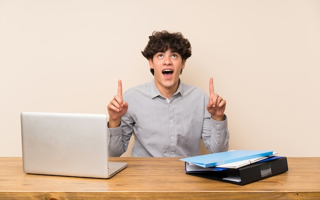 Jeune étudiant avec un ordinateur portable surpris et pointant vers le haut Photo Premium