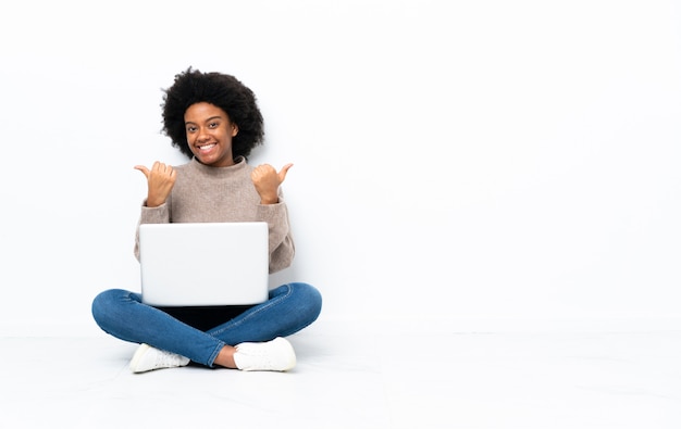 Jeune Femme Afro Américaine Avec Un Ordinateur Portable Assis Sur Le Sol Avec Le Geste Du Pouce 