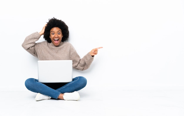 Jeune Femme Afro Américaine Avec Un Ordinateur Portable Assis Sur Le Sol Surpris Et Pointant Le 