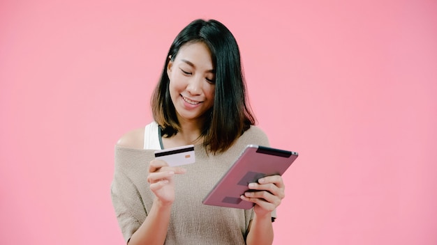 Jeune femme asiatique à l'aide d'une tablette, achat en ligne shopping par carte de crédit, sentiment heureux souriant dans des vêtements décontractés sur fond rose studio shot heureuse femme heureuse souriante adorable se réjouit du succès. Photo gratuit