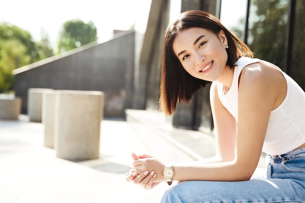 Jeune Femme Asiatique Assise Sur Un Banc Prs Du Btiment Souriant