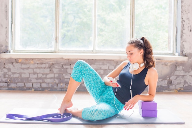 Jeune femme assise sur un tapis d'exercice à l'aide de smartphone Photo gratuit