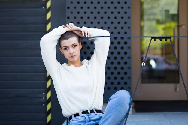 Jeune Femme Aux Cheveux Courts Assis Contre Un Bâtiment