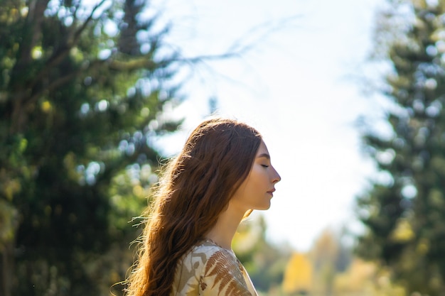 Jeune femme aux longs cheveux roux vêtue d'une robe en lin cueillant des champignons dans la forêt Photo gratuit