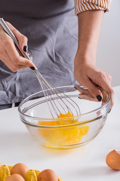Jeune femme battant le jaune d'oeuf dans le bol en verre avec un fouet sur un tableau blanc Photo gratuit