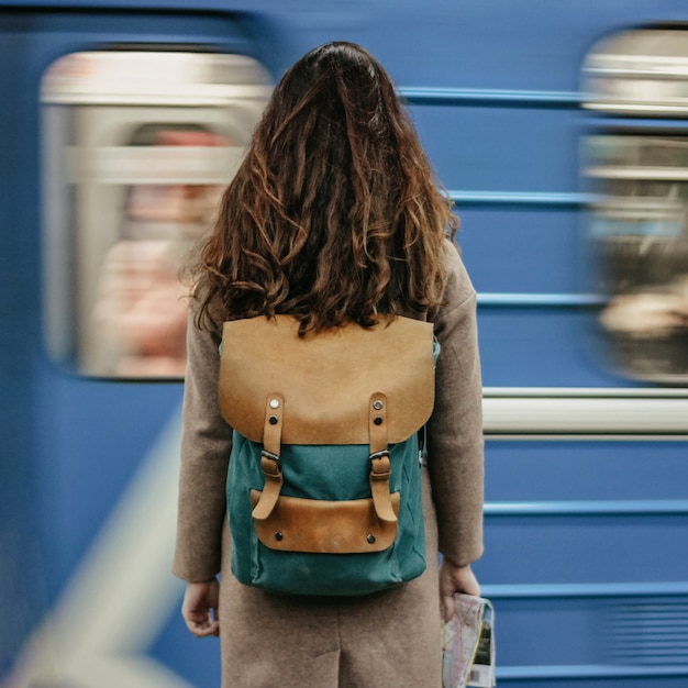 Jeune femme bouclée voyageuse tête rouge avec sac à dos et carte dans la station de métro en face du train Photo Premium